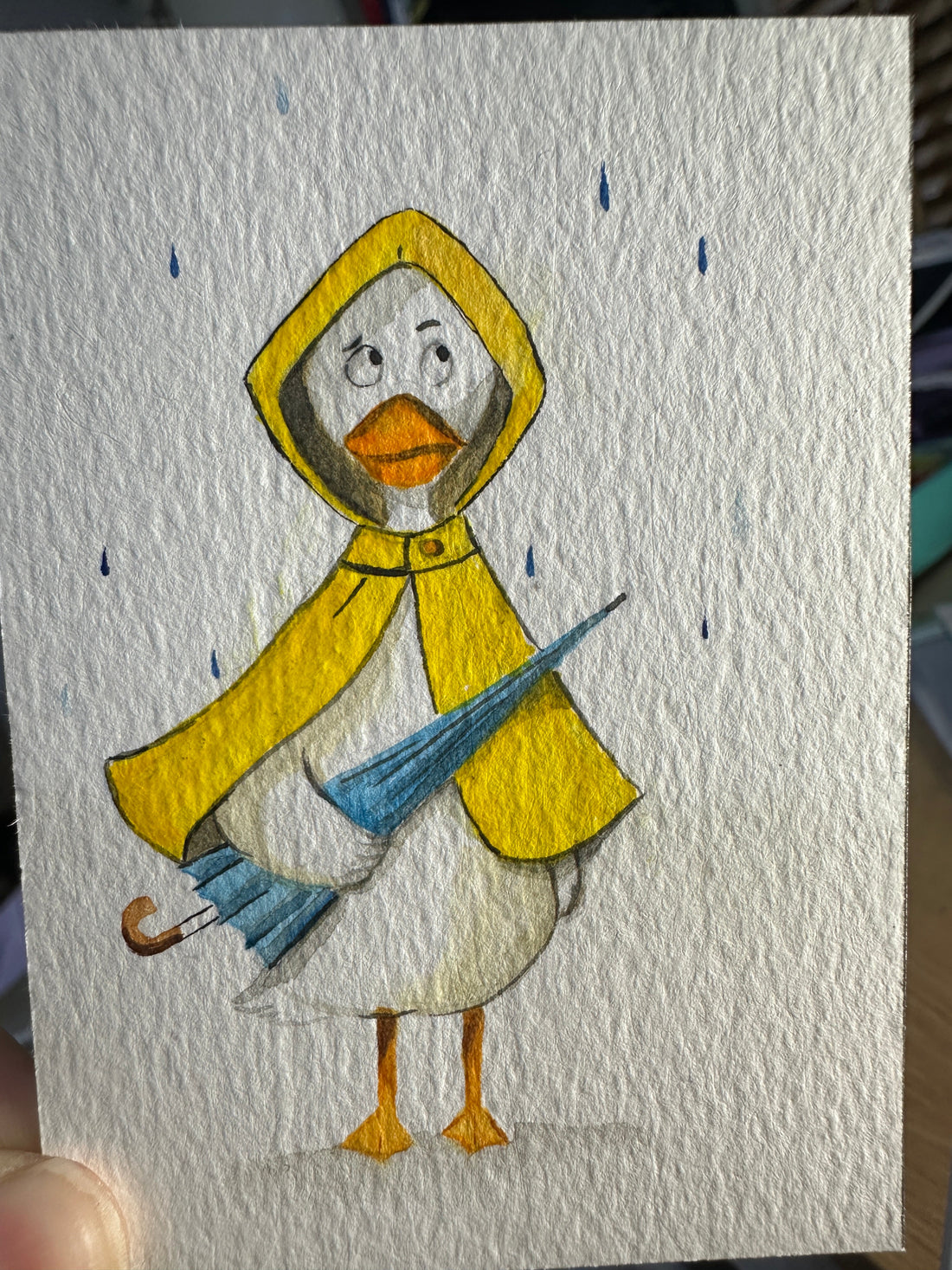 Original ACEO watercolor and gouache painting of a duck in a yellow raincoat holding a blue umbrella in the rain