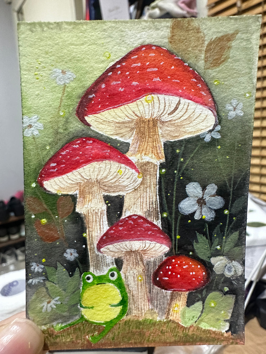 Original ACEO watercolor and gouache painting of a frog sitting beneath red-and-white toadstool mushrooms in a forest