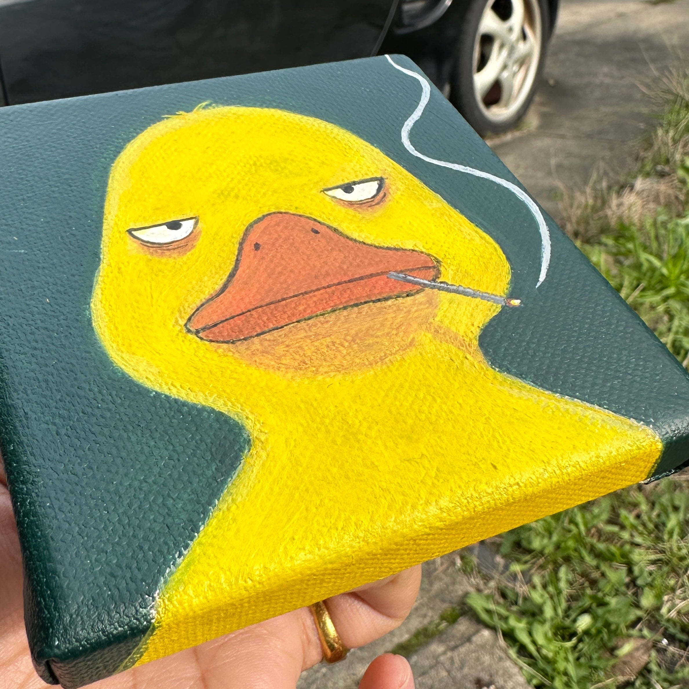 Angled view of the duck with cigarette canvas painting held in hand outdoors